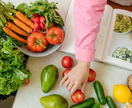 Top view of fresh vegetables and hands arranging them with a recipe book, promoting healthy eating.